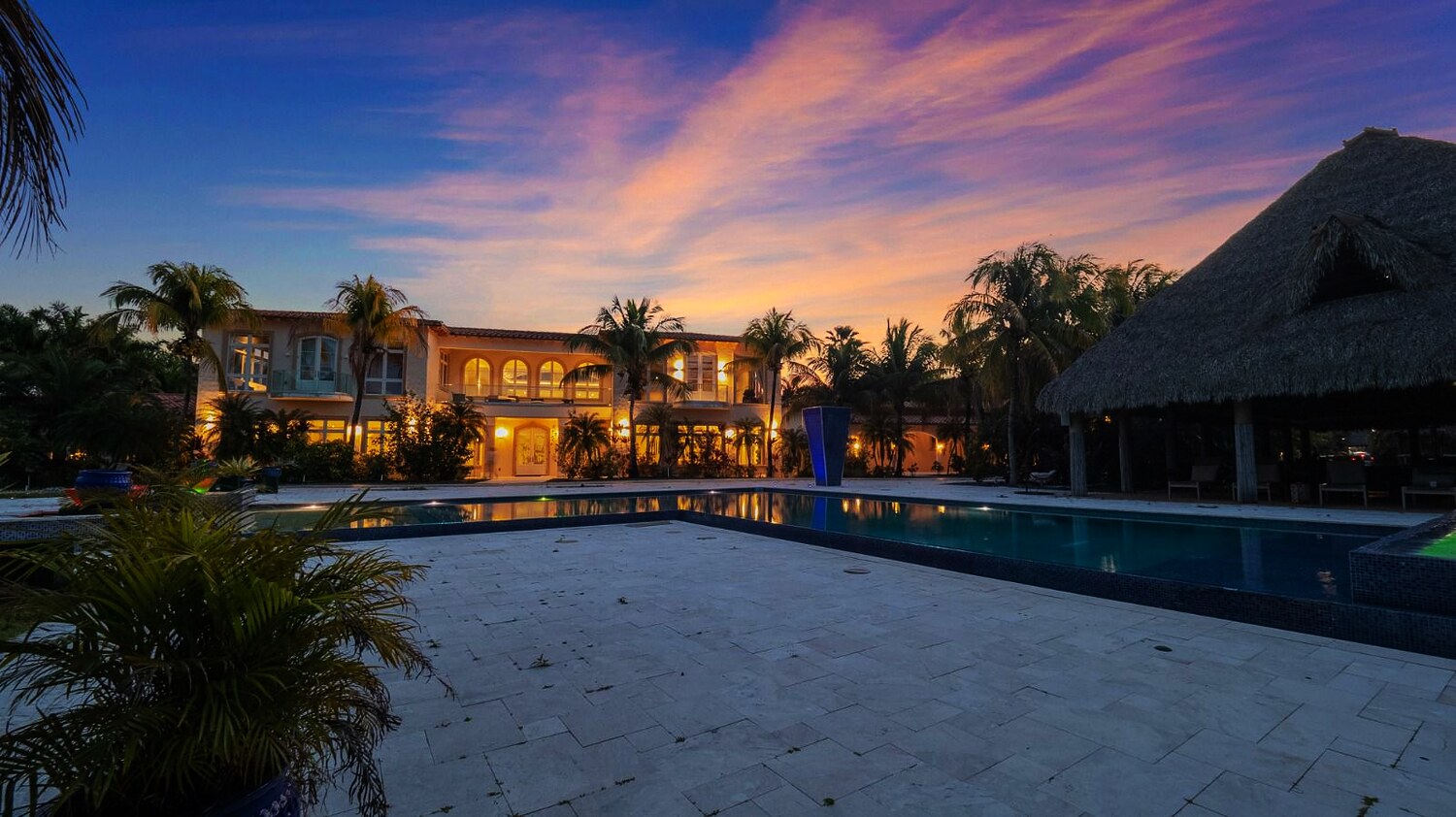 A private waterfront estate at dusk, lit above its pool and cabana